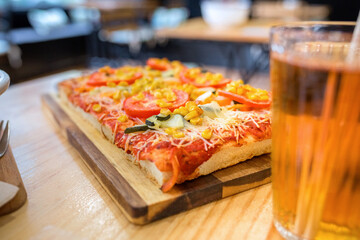 Close up of vegetarian focaccia with melted cheese, tomato, zucchini, and corn kernels, being served with an iced tea drink over wooden table on restaurant. Healthy and organic fast food concept.