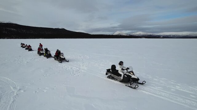 An aerial following a line of tourists on snowmobiles as they ride across the vast frozen surface of Fish Lake near Whitehorse, Yukon, Canada