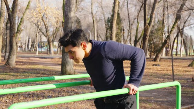 Man doing dips on parallel bars at outdoor sports ground.