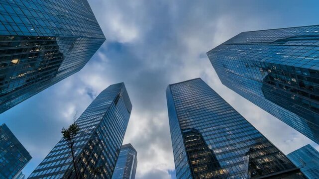 Fast clouds race behind modern skyscrapers from low angle creating dynamic urban time lapse energy movement scale contrast