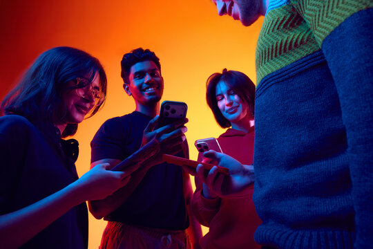 Friends checking smartphones in colorful studio lighting. Concept of mobile app advertising, digital communication promotion, youth marketing campaigns, and tech branding.