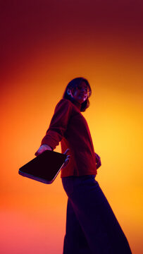 Woman presenting smartphone screen in dynamic pose in neon lightning. Concept of mobile advertising creatives, app promotion visuals, digital campaign design, and tech marketing content.