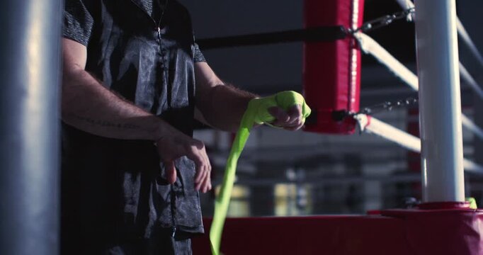 Close-up 4k video of a male fighter wrapping green hand bandages for boxing workout. Focused and steady, the boxer wraps bright yellow hand wraps, gearing up for rigorous training.