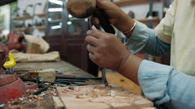Close up of a carpenter using a chisel and mallet to carefully carve an intricate design into a wooden plank in a workshop, Siem Reap, Cambodia.