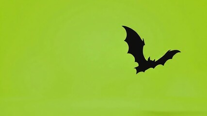 Silhouette of a black nocturnal bat flapping its wings while flying through the air isolated on a solid green screen for easy chroma keying