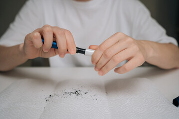 Person hands disassembling tobacco heating device to clean accumulated residue, performing regular maintenance for electronic cigarette system on paper towel, close-up cropped shot.