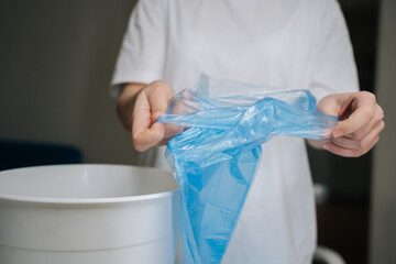 Hands unfolding and positioning fresh blue plastic bag into empty white trash can, signifying start of efficient waste management and cleanliness routine in domestic setting, close-up cropped shot.