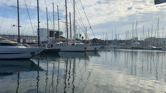 Sailboats and industrial port at Barcelona harbor with calm water reflections