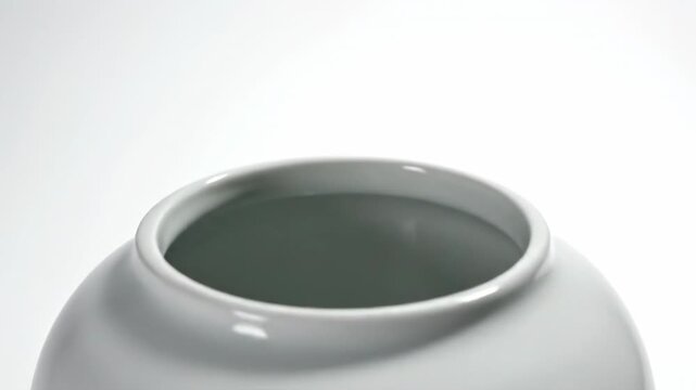 Wide high key studio shot of an empty cylindrical porcelain vase casting subtle shadow texture onto a bright white surface against a clean background