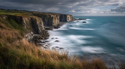 Coastal landscape showcases cliffs, water, and sky under a dramatic, cloudy sky