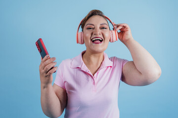 portrait of adult latin woman listening to music and using headphones while holding mobile phone on...