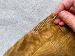 Close-up of hand sewing corduroy trousers to adjust the waist size.