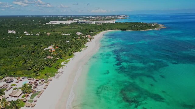Aerial footage pulling back along a tropical coastline at Xpu-Ha near Tulum, Mexico, revealing Caribbean waters, white sand beach, lush jungle, and the Barcelo Maya Grand resort complex