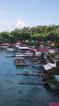 Vertical aerial dolly forward shot showcasing Bastimentos Island&rsquo;s picturesque coastline with vibrant homes and lush greenery by the water in Panama.