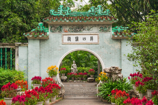The beautiful chinese circle entrance gate into Lou Lim Ieoc public garden with sculpture of young woman and crane surrounded by lush and bright flowers and green leaves. Macau, China