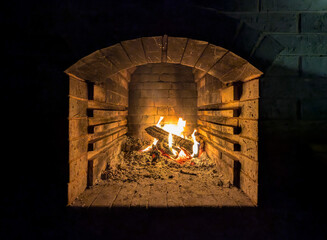 Baking of flat pita bread in wood-fired oven on local street market. Firewood with fire creates light that fills the large volume of the brazier