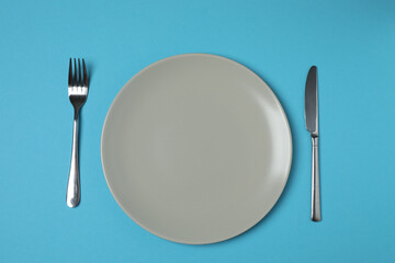 Empty plate and cutlery on colored background, top view
