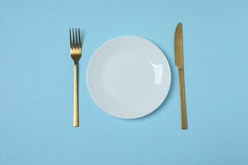 Empty plate and cutlery on colored background, top view

