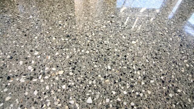 Reflective Terrazzo Floor with Window Shadow. Close-up of a polished terrazzo floor featuring a speckled pattern in shades of gray, black, and white. The glossy surface reflects a multi-pane window