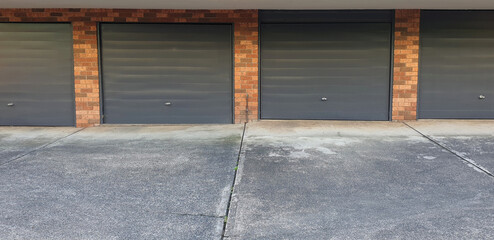 four grey colour single parking garage doors in a row against old brick wall on building