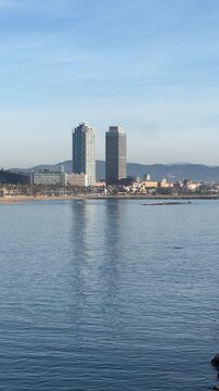 Calm sea view of Barcelona waterfront skyline with modern towers reflected on the water, coastal city landscape and urban beach area under clear sky, Mediterranean travel destination and everyday city