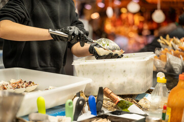 Unrecognizable person wearing gloves scooping cooked octopus into small cups at a market © Carlos