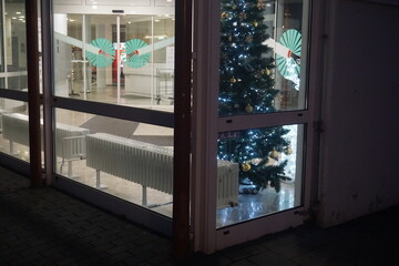 Beleuchteter Eingangsbereich von Krankenhaus mit Glasfassaden und geschm&uuml;ckten Christbaum im Innenraum in der Nacht im Winter