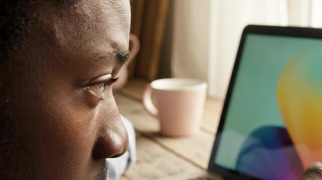 Close-up of a man's face looking intently at a laptop screen, with a coffee cup in the background, highlighting focus and digital engagement