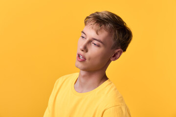Fototapeta premium Young man wearing a yellow shirt against a vibrant yellow backdrop, thoughtful expression, casual studio shot highlighting mood, color harmony, and soft lighting for lifestyle imagery