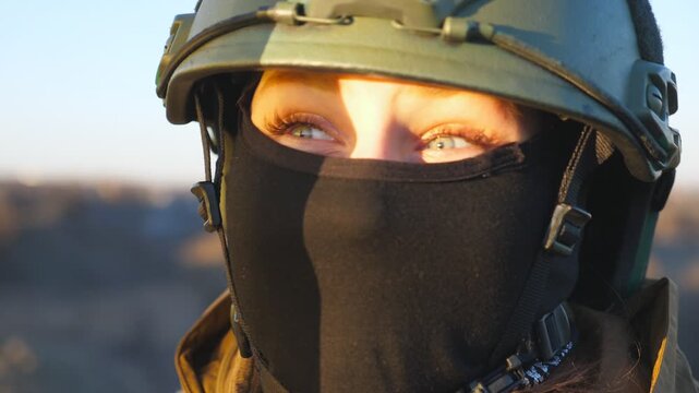 Portrait of young military woman in helmet and balaclava at countryside. Sight of female ukrainian army soldier outdoor. Concept of peace and support against russian aggression. Invasion resistance