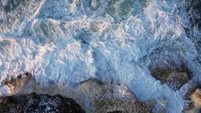 Aerial view of powerful waves as they crash against the rocky coast, creating a dynamic interplay of white foam and dark stone, Lozenets, Tsarevo, Bulgaria.