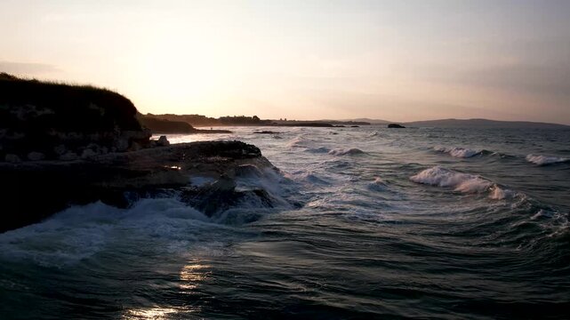 Aerial view of waves crashing against the rocky coast, creating a dynamic interplay of dark blues and whites under the fading light, Lozenets, Tsarevo, Bulgaria.