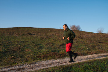 A bearded middle-aged man exercises on a sports ground in a park using exercise equipment, jogging on rough terrain, morning run