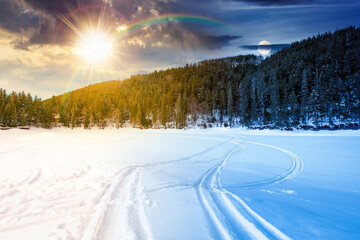 snow covered frozen lake in natural park. day and night time change concept. winter solstice landscape surrounded with coniferous forest in mountains with sun and moon. harmony and progress calendar