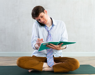 Positive young student talking on a mobile phone and making notes in notebook