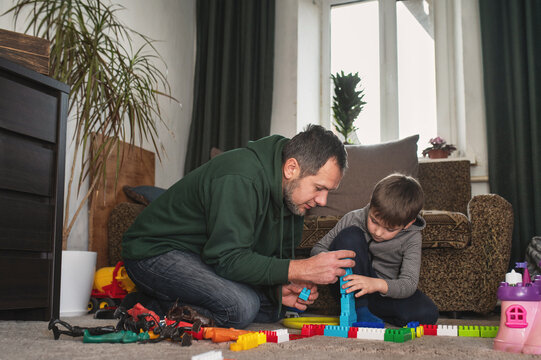 Father and son build a tower from a plastic construction set at home, dad teaches the child and plays with him
