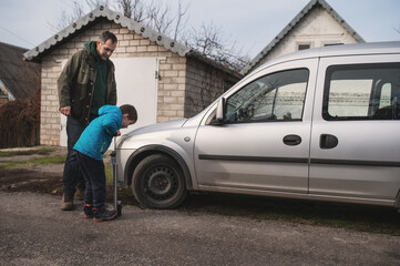 A father and son pump up a car tire with a hand pump. A little helper, a father teaching his son about manly things.