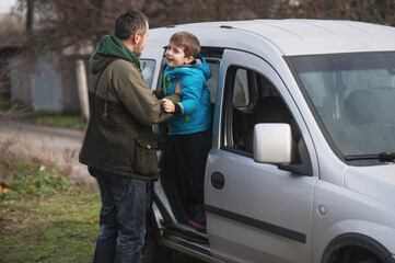 A father helps his young son out of the car, spending time together and relaxing on the road. Father and child have a good time together.