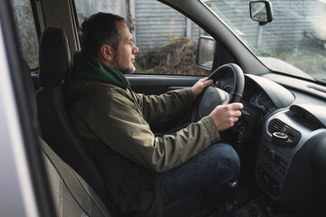 A bearded man in a windbreaker jacket driving a car © illustrissima