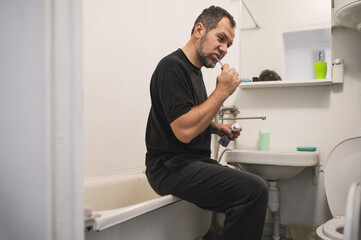 A bearded man brushes his teeth in the bathroom near the mirror, daily self-grooming