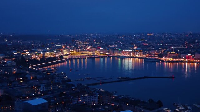 Aerial view of city lights twinkling and reflecting on the dark water, creating a mesmerizing contrast of light and shadow, Rade of Geneva, Geneva, Switzerland.