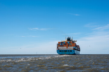 A large container ship seen from behind, with many seagulls near the ship.