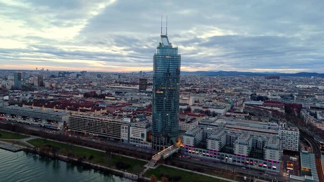 Aerial drone shot panning left toward the Vienna Millennium Tower, showing the skyscraper rising above surrounding city buildings, winter clouds overhead, and muted winter light on streets