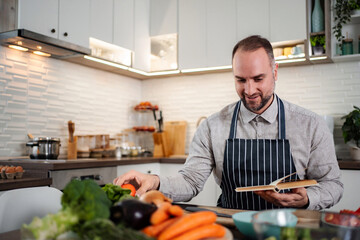 Man in apron preparing fresh vegetables following recipe book