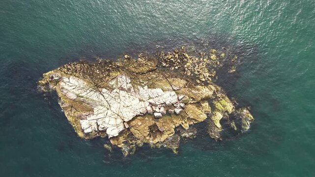 Aerial view of Dalkey Island's rocky outcrop, a stark contrast of white and gold rocks against the deep turquoise sea, Dalkey Island, County Dublin, Ireland.