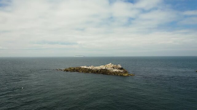 Aerial view of a rugged, rocky island, its white and brown rocks contrasting with the deep blue sea under a cloudy sky, Dalkey, County Dublin, Ireland.