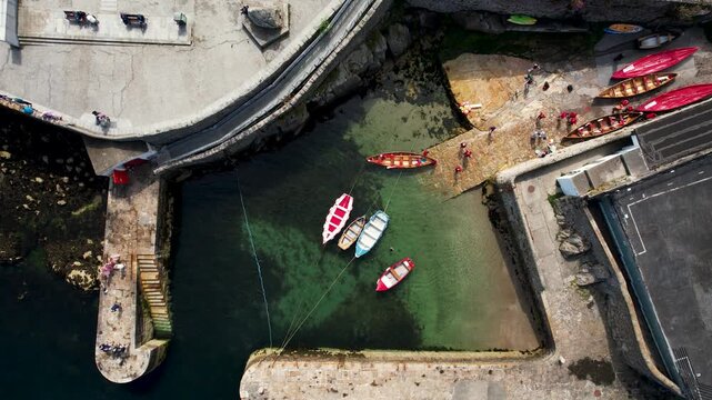 Aerial view of colourful boats bobbing gently in the clear waters of Dalkey harbour surrounded by stone piers and people, Dalkey, County Dublin, Ireland.