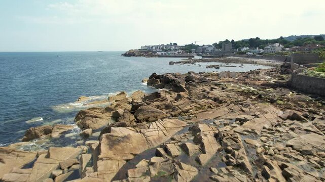 Aerial view of the rugged Dalkey coastline where the dark blue sea meets the rocky shore and town buildings, creating a striking contrast, Dalkey, County Dublin, Ireland.