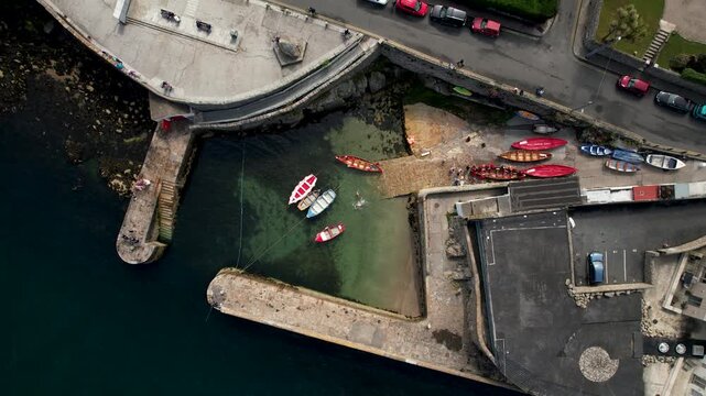 Aerial view of Dalkey Harbour with boats floating on the clear water surrounded by stone jetties, a coastal road, and buildings, Dalkey, County Dublin, Ireland.