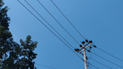 Electric utility pole with power lines crossing a clear blue sky. Urban electricity infrastructure, energy distribution cables, minimal outdoor scene, technology and connection concept